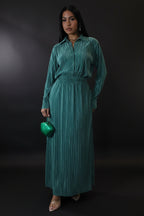 Woman wearing a teal dress holding a green handbag against a plain background
