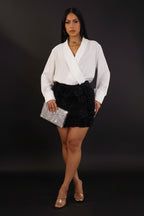 Woman wearing a white blouse and black floral skirt with a silver clutch against a plain background