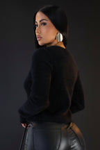 Woman wearing a black sweater and black pants against a plain background